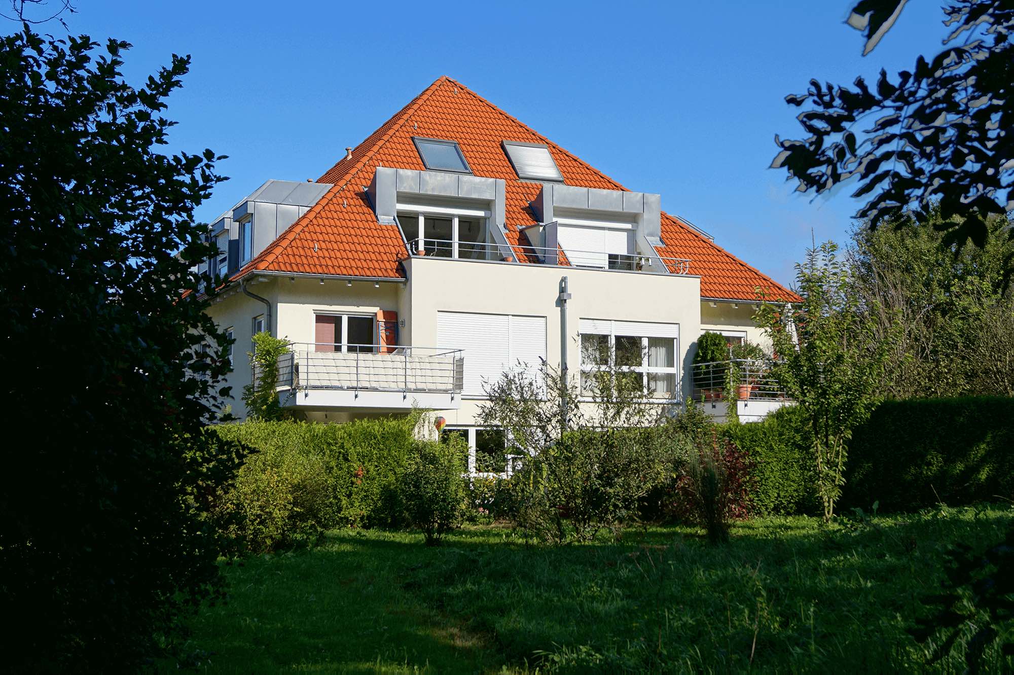 Moderne Wohnanlage mit rotem Satteldach und großzügigen Balkonen, umgeben von gepflegtem Garten in Ravensburg – ideal für den Kauf eines Hauses.